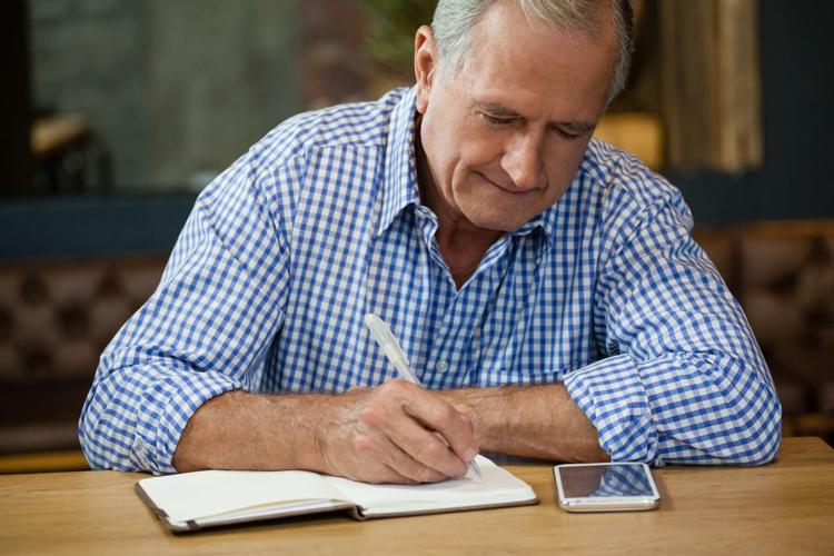 Senior man writing on diary at table