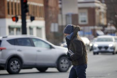 man crosses traffic bracing against cold and wind