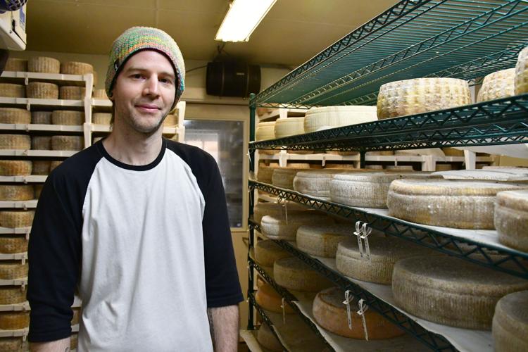 A man stands in a fridge with rounds of cheese