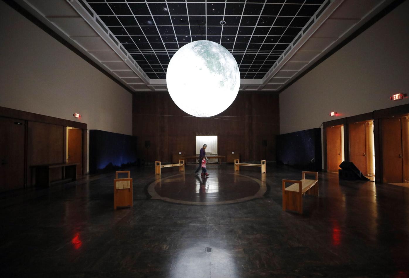people walk under large moon in gallery