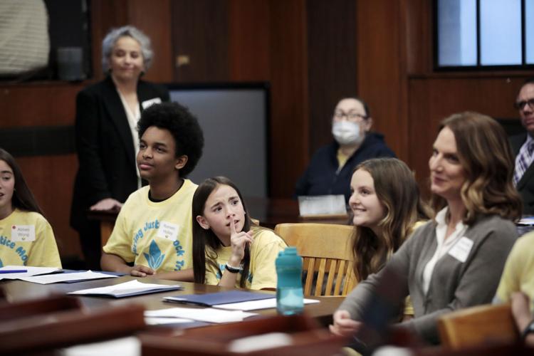 girl at table of kids in courtroom leans over to shush others with finger