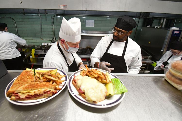 A chef and student chat with two sandwiches in the foreground