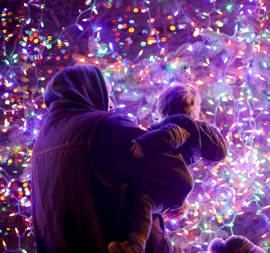 father holds son looking at lit tree