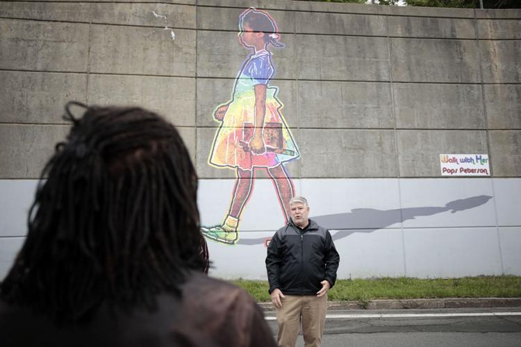 man speaks in front of rainbow mural