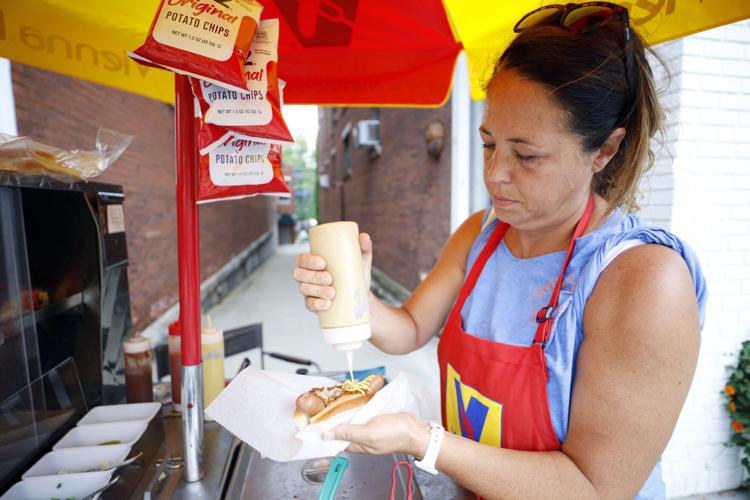 woman squeezes mustard onto hot dog at hot dog cart