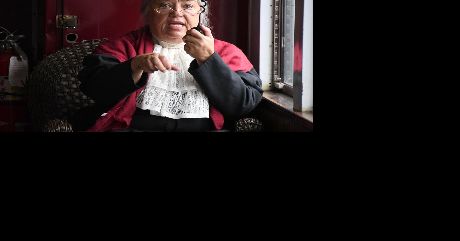 A woman in period clothing speaks on a train