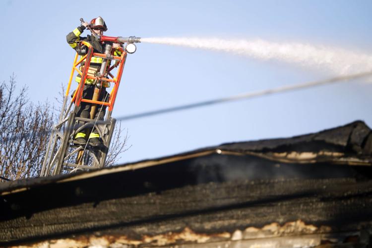firefighter adjusts water hose on ladder