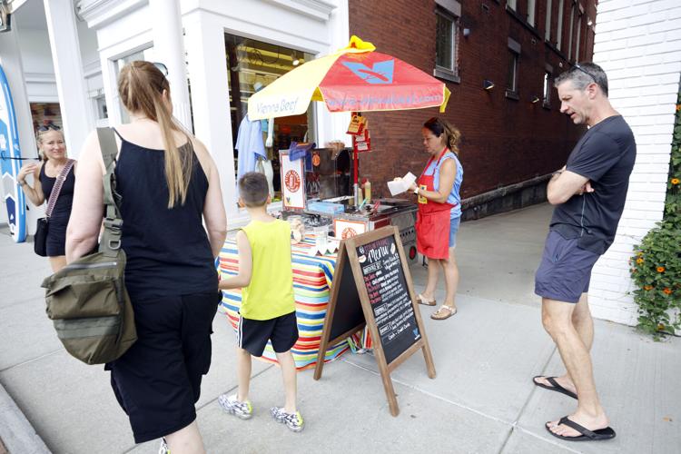 crowd looks at hot dog stand on sidewalk