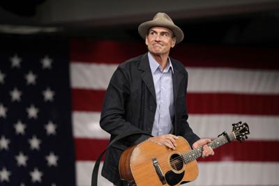 James Taylor holding guitar in front of American flag