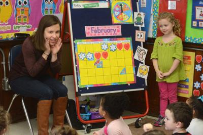 Teacher next to colorful board with month on it talking to students