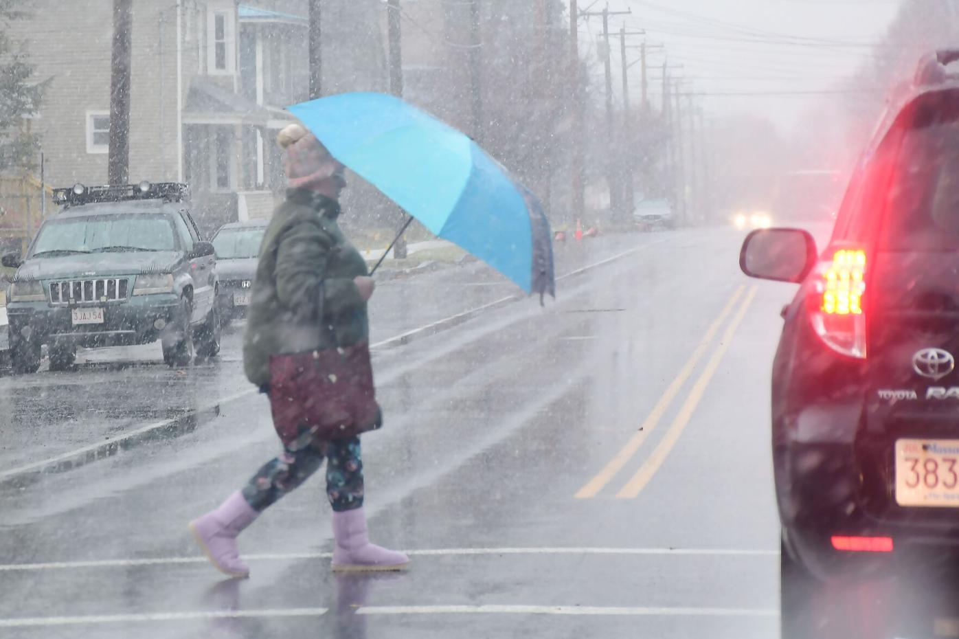 Holding an umbrella, a woman crosses the street
