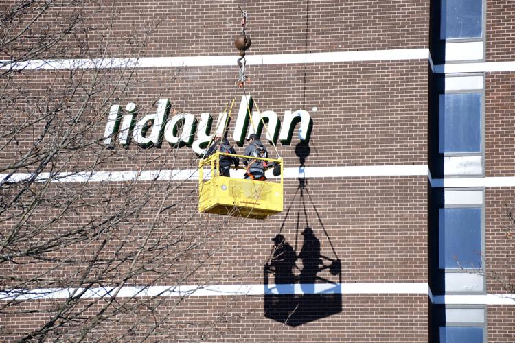 Men in a crane lift take down the sign of the former Holiday Inn