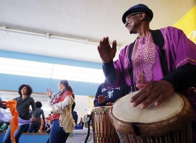 Man in purple shirt and black fedora leads a drum circle