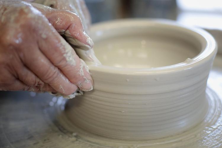 hands squeezing clay into a bowl on pottery wheel