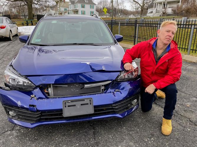 Christopher Brophy kneels by his damaged car