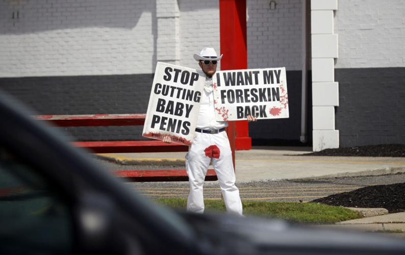 man in white with red stain on pants protesting circumcision