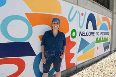 An artist stands in front a mural