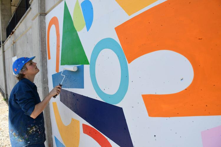 An artist uses a roller to put a sealant on a mural