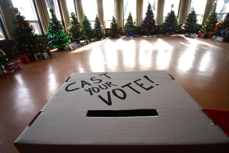 A room full of decorated holiday trees with a box that says "cast your vote!"