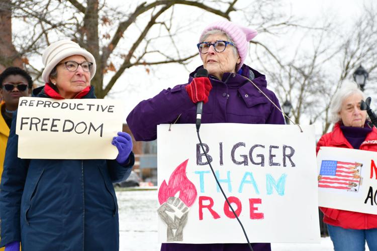 Two women hold signs and one speaks at a rally