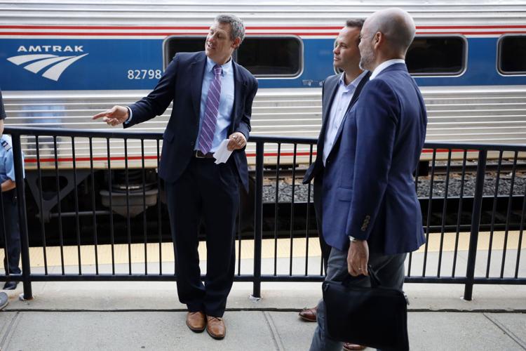 three men talking in suits in front of train
