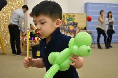 Max Chen blows on a pinwheel with a balloon animal at the Guidepost Montessori open house in April. Photo by Jesse Wright