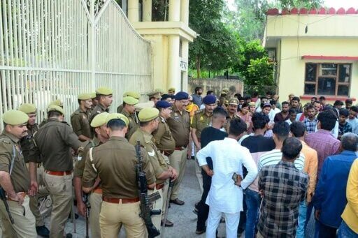 Policemen stand guard as mourners protest after newborns died in a hospital blaze in Jhansi