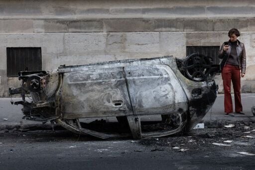 A woman takes a photo of the wreckage of a burnt-out car in central Paris