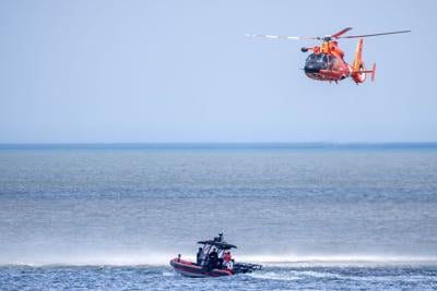 A bright orange helicopter above the water and rescue boat on the water.