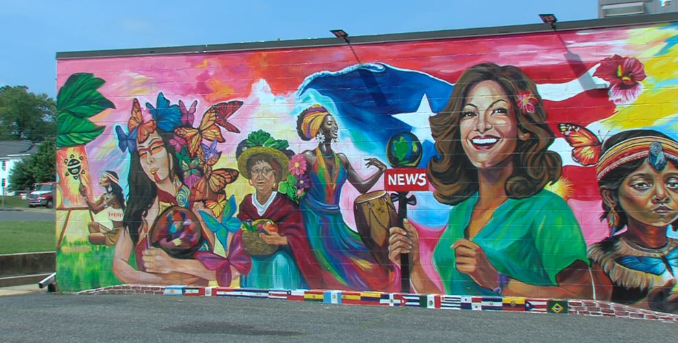 A mural showing a woman painting, a woman whose head is covered in butterflies, a lady carrying a basket of fruit, a news reporter on a colorful background.