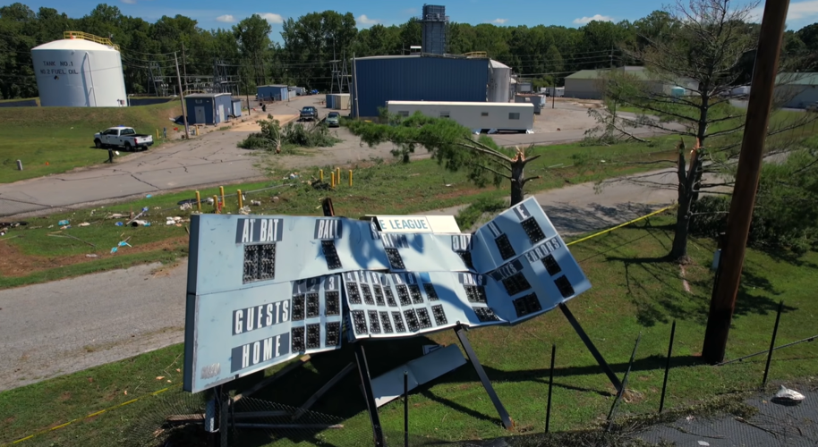 A scoreboard for little league baseball barely stands, heavily damaged.