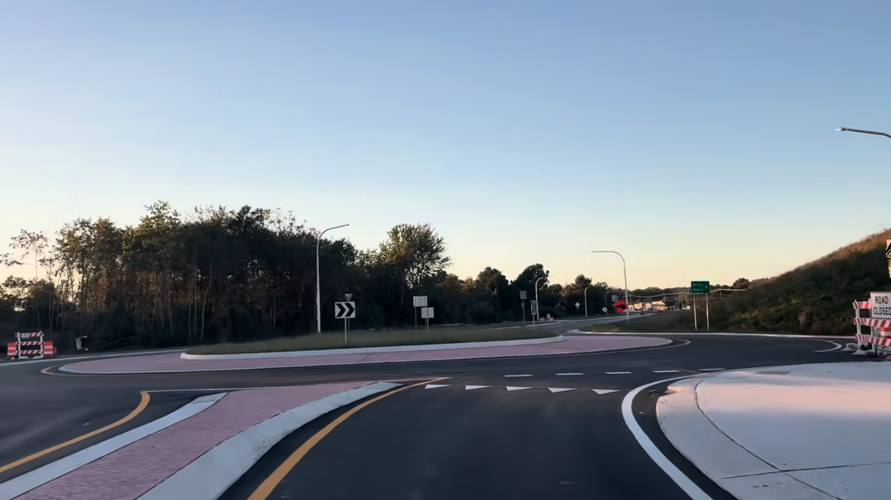 A picture from a drivers point of view with no cars in the roundabout fresh pavement and paint pointing drivers to the roundabout.