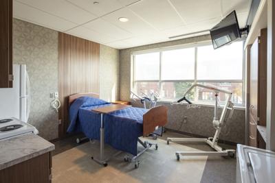 A room with a hospital bed, tv, tray, and fridge with three open windows.