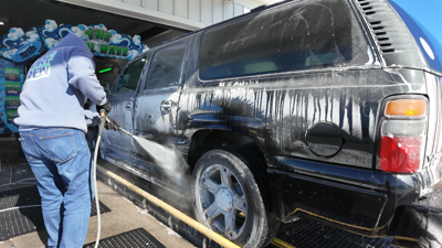 A worker sprays down an SUV at a car wash.