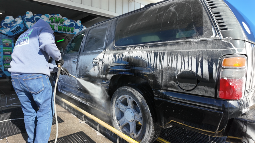 A worker sprays down an SUV at a car wash.