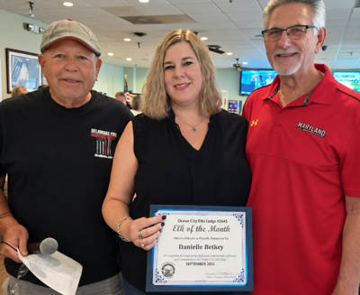 three people pose for a photo as the woman named elk of the month holds the certificate 