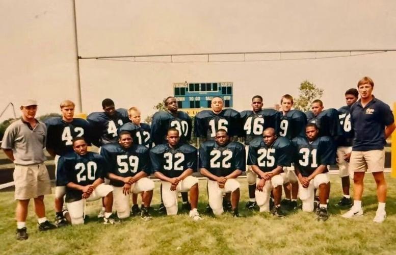 Football players and coaches pose, lined up along a football field.