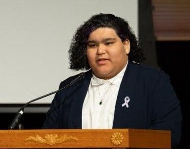 They stand at a podium with a ribbon pin on the lapel.