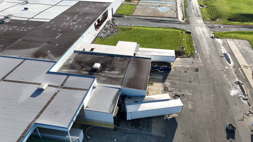 An aerial view of walls down on a large building and turned over tractor trailers.