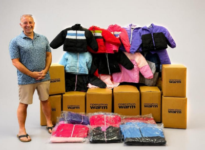 A man stands besides several boxes and children's winter coats.