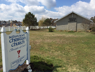Church on grass and accompanying sign. 