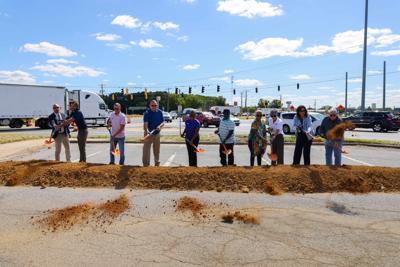 Several people line up along a pile of dirt with shovels.