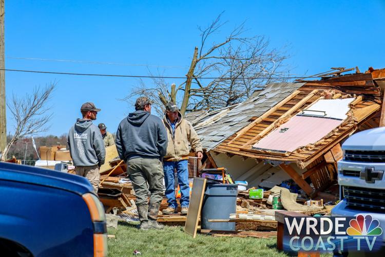 Men cleaning up stand near a large piece of a damaged structure.