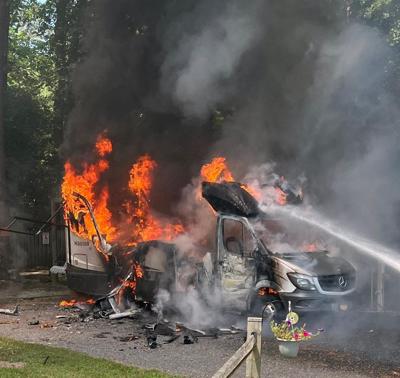 A recreational vehicle completely engulfed in flames with water being sprayed from the right side of the photo.