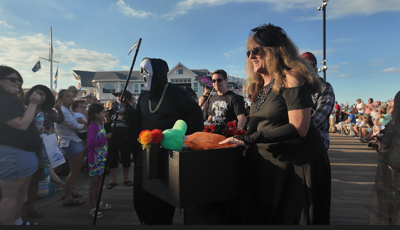 People dressed in Halloween type costumes walking a coffin down the boardwalk