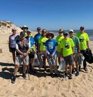 A group of volunteers with bags pose on the beach.