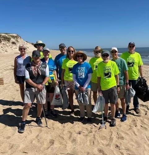 A group of volunteers with bags pose on the beach.