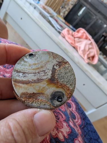 A small round rusty object held up by a person's fingers.