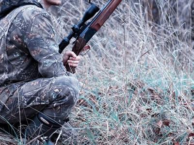 A hunter squatting down in the woods.