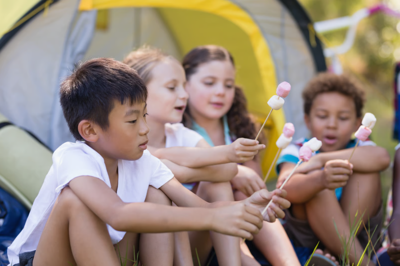 Four kids roasting marshmallows with yellow tent in background